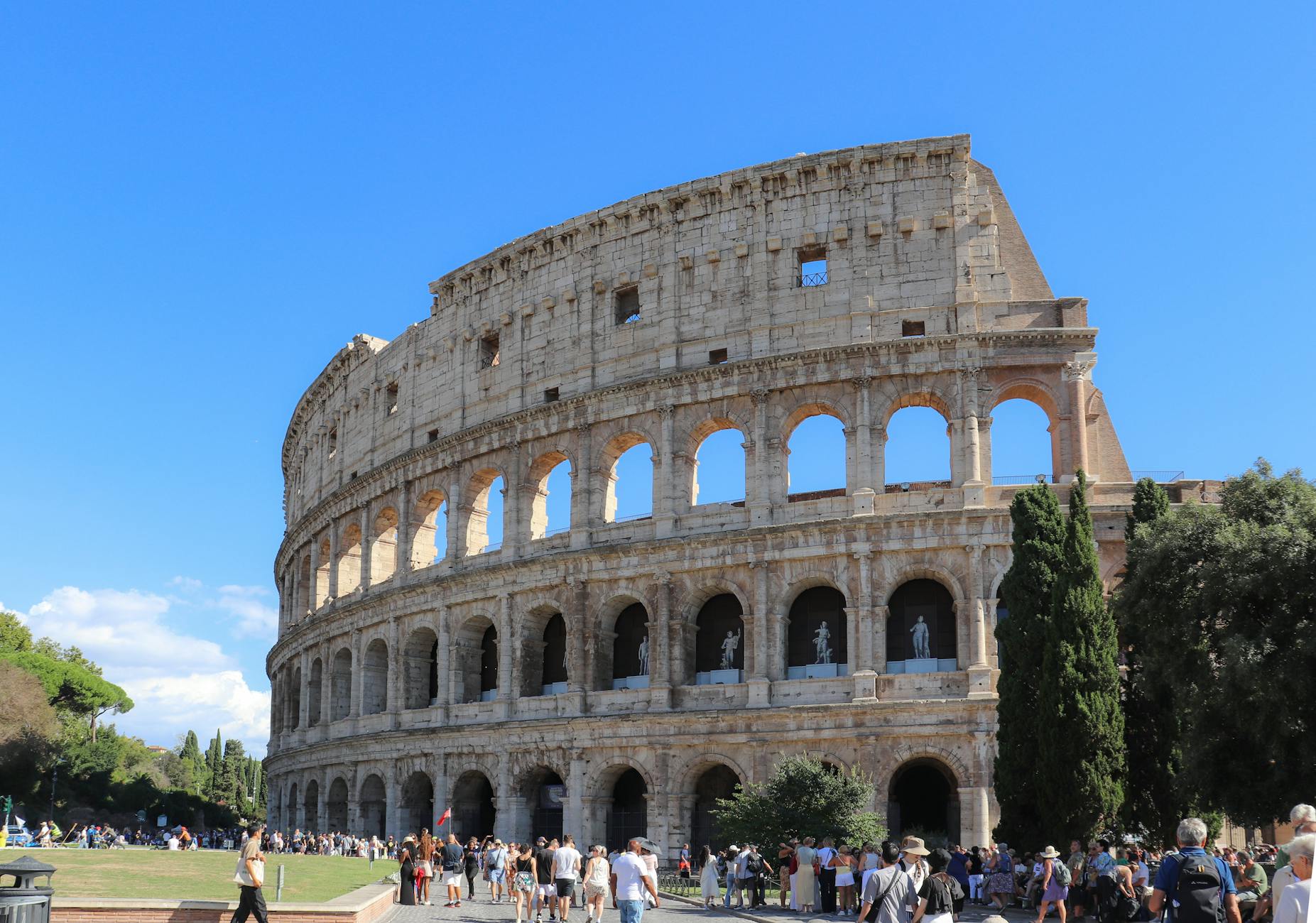 colosseum in rome with tourists under blue sky