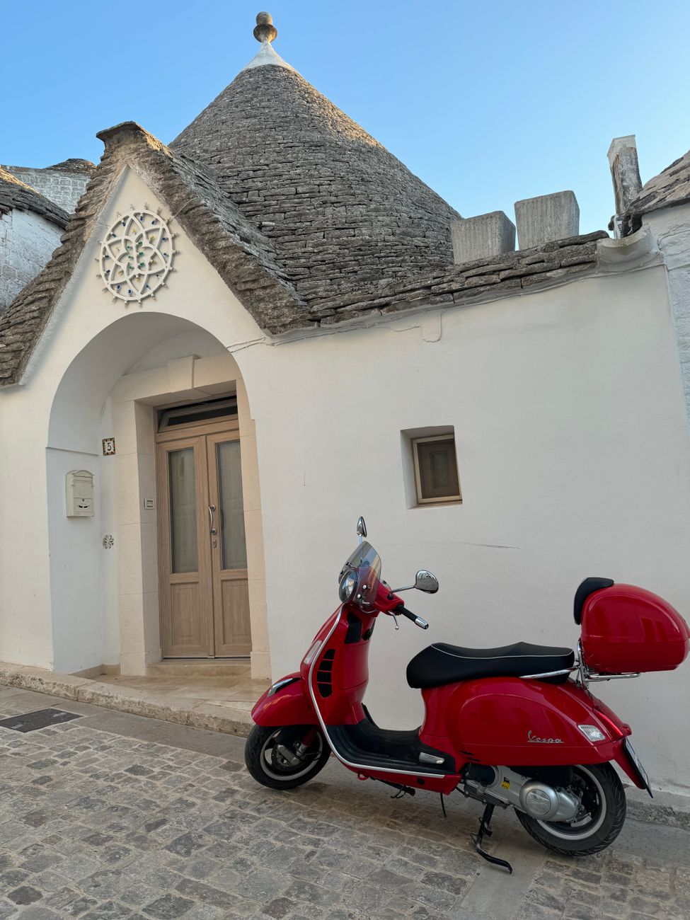 red vespa in front of traditional trullo house